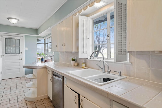 kitchen with tile countertops, a healthy amount of sunlight, a sink, stainless steel dishwasher, and tasteful backsplash