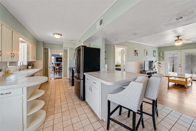 kitchen with visible vents, a sink, freestanding refrigerator, a peninsula, and tile counters