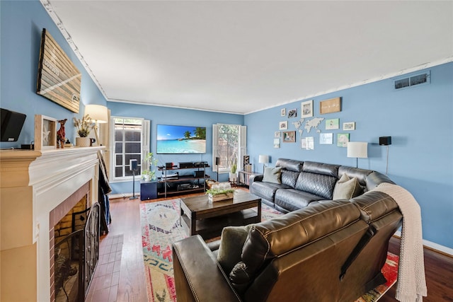 living room featuring visible vents, a fireplace, baseboards, and wood finished floors