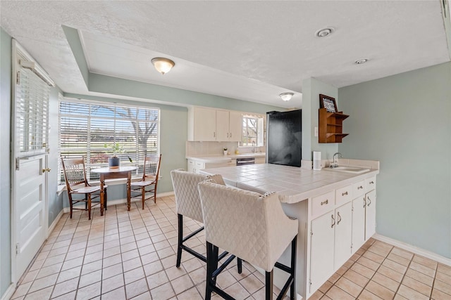 kitchen featuring a breakfast bar, a sink, tile countertops, a peninsula, and light tile patterned flooring