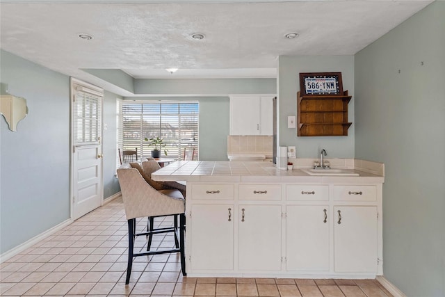 kitchen featuring tile counters, white cabinets, baseboards, and a sink