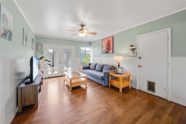 living area featuring crown molding, ceiling fan, a wainscoted wall, french doors, and wood finished floors