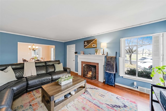 living room featuring a notable chandelier, a brick fireplace, wood finished floors, and ornamental molding