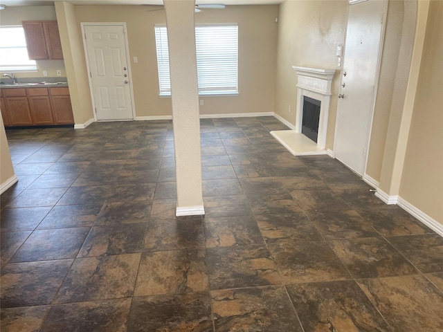 unfurnished living room featuring a fireplace with raised hearth, stone finish flooring, baseboards, and ceiling fan