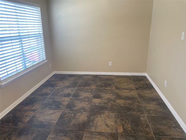 unfurnished room with stone finish floor and baseboards