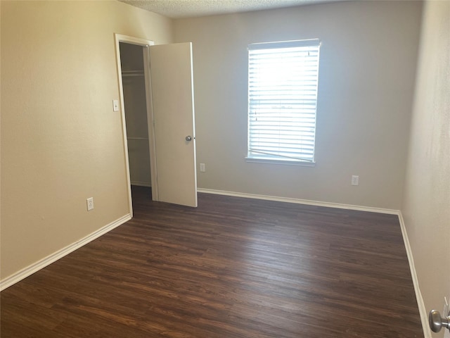 spare room featuring a textured ceiling, dark wood-type flooring, and baseboards