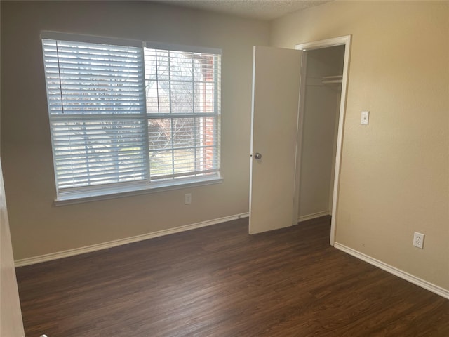 unfurnished bedroom featuring a closet, baseboards, a textured ceiling, and dark wood-style flooring