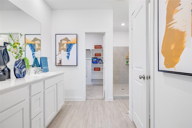 bathroom featuring vanity, wood finished floors, a walk in shower, and baseboards