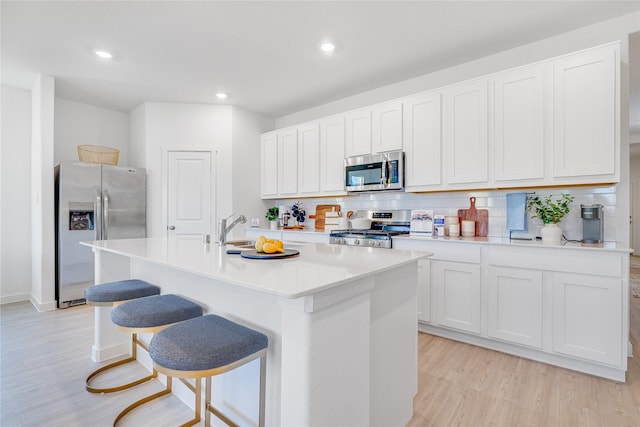 kitchen with a kitchen island with sink, light wood-style flooring, a sink, stainless steel appliances, and decorative backsplash