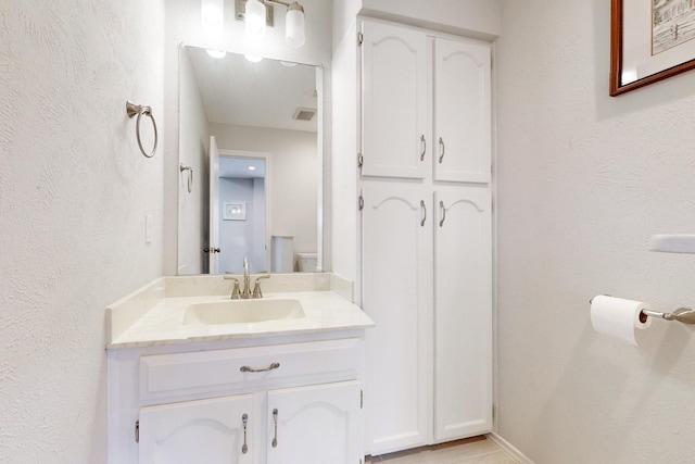 bathroom with visible vents, toilet, vanity, and a textured wall