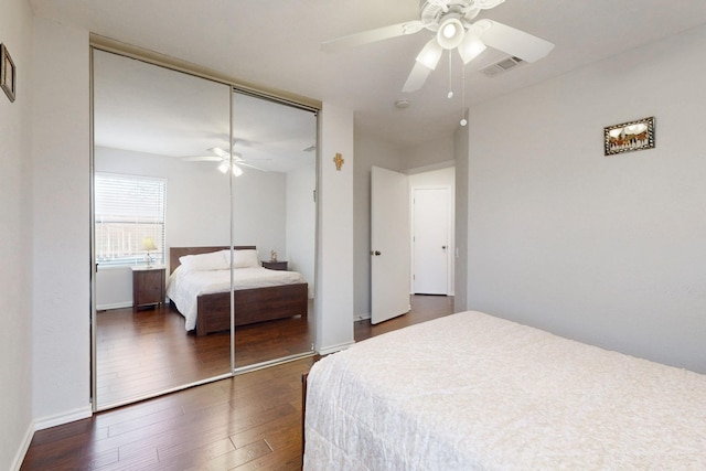 bedroom with baseboards, visible vents, dark wood finished floors, ceiling fan, and a closet