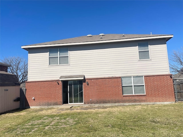 back of house featuring brick siding, a lawn, and fence