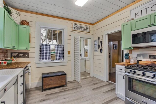 kitchen with green cabinetry, stainless steel appliances, wooden walls, and light wood finished floors