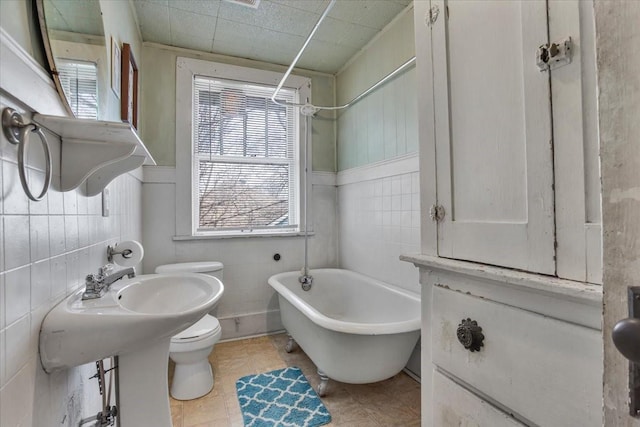 bathroom with a soaking tub, toilet, and tile walls