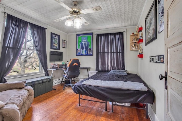 bedroom featuring wood-type flooring, ornamental molding, and a ceiling fan