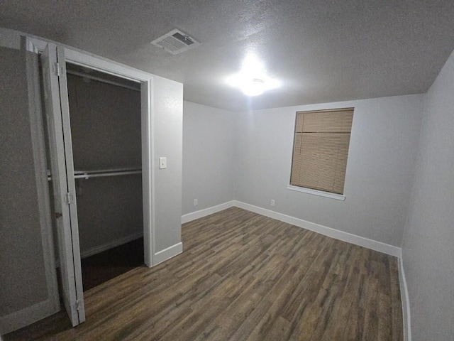 unfurnished room with visible vents, a textured ceiling, dark wood-type flooring, and baseboards