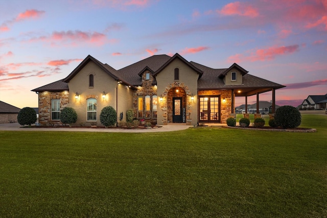 french country home featuring a lawn, stone siding, and french doors