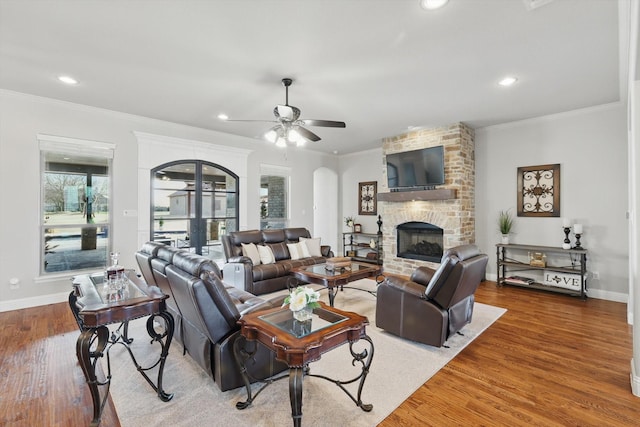 living area featuring ornamental molding, wood finished floors, arched walkways, and a large fireplace