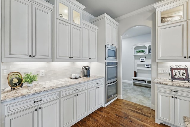 kitchen with arched walkways, glass insert cabinets, appliances with stainless steel finishes, crown molding, and backsplash