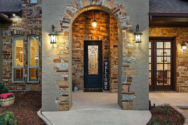 view of exterior entry with brick siding, stone siding, and a shingled roof