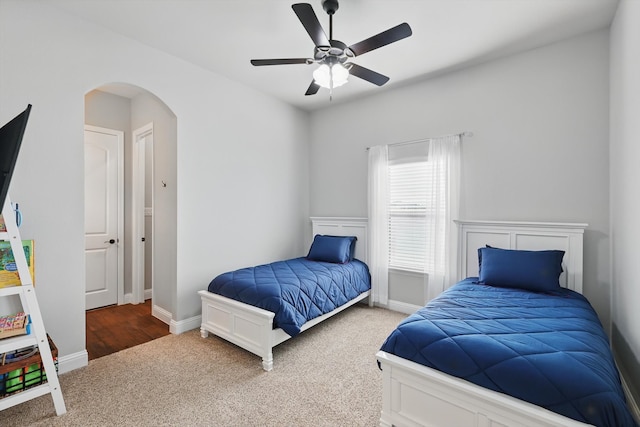 carpeted bedroom with baseboards, arched walkways, and ceiling fan