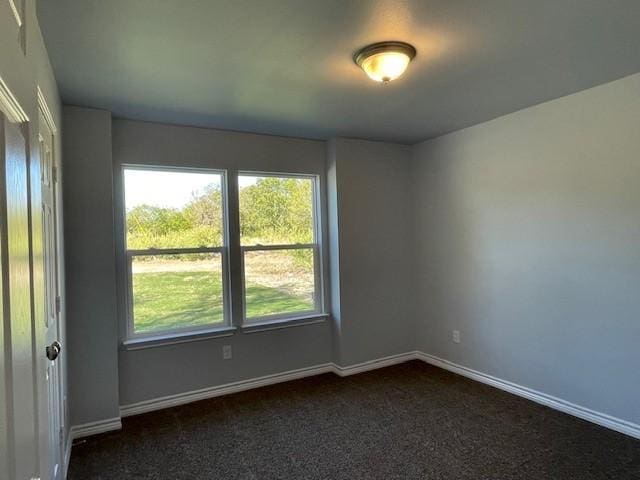 unfurnished room featuring baseboards and dark colored carpet