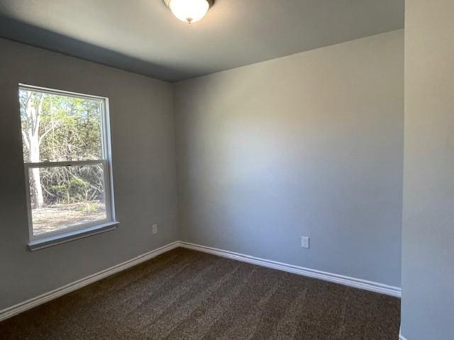 empty room featuring baseboards and dark colored carpet