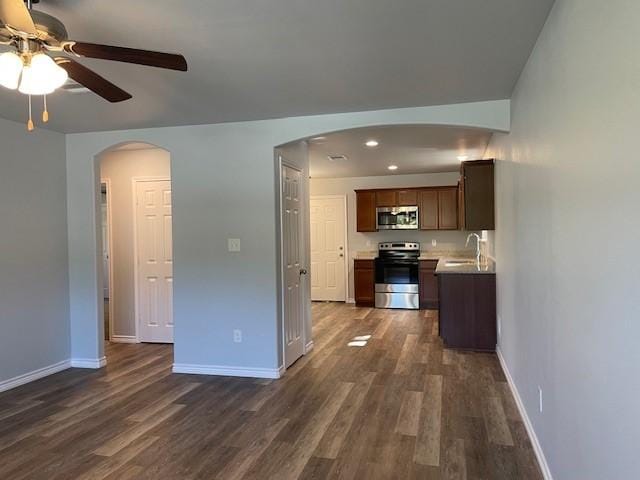 unfurnished living room with dark wood finished floors, baseboards, arched walkways, and a sink