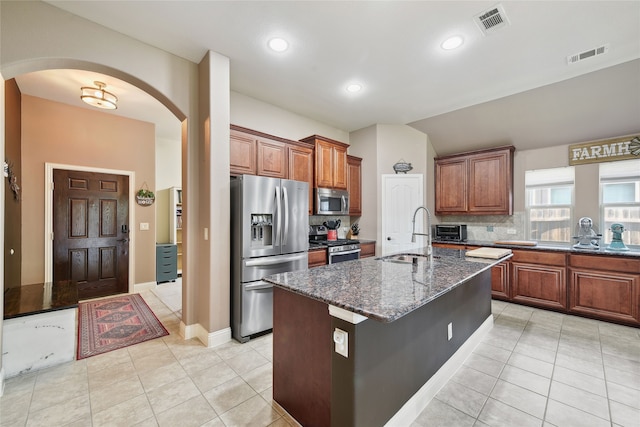 521 Eastbrook Dr, Anna, TX 75409 - kitchen featuring stainless steel appliances, arched walkways, dark stone counters, light tile patterned flooring, and brown cabinetry