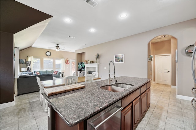 kitchen featuring visible vents, dishwasher, a fireplace, arched walkways, and a sink