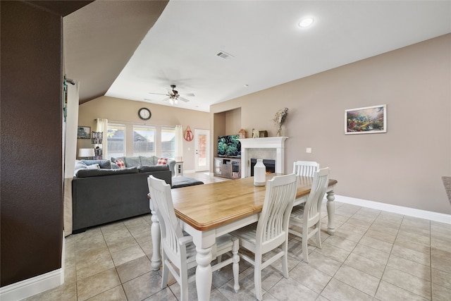 dining room with light tile patterned floors, baseboards, lofted ceiling, a warm lit fireplace, and ceiling fan