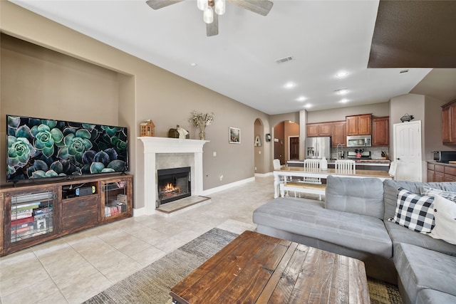 living area featuring visible vents, baseboards, a warm lit fireplace, light tile patterned flooring, and arched walkways