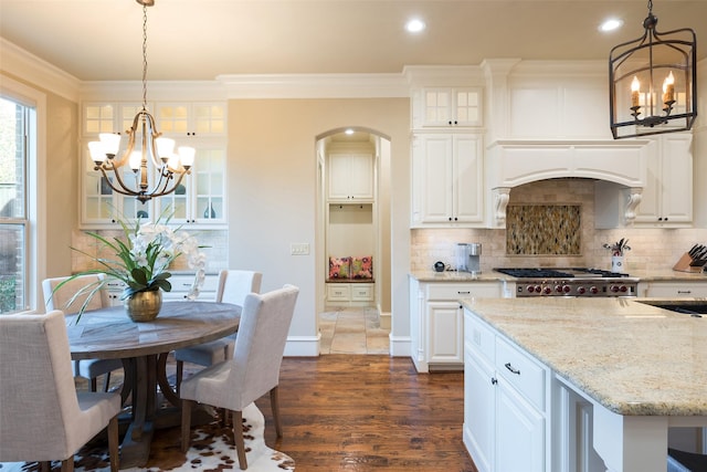 kitchen featuring light stone countertops, an inviting chandelier, ornamental molding, stove, and backsplash