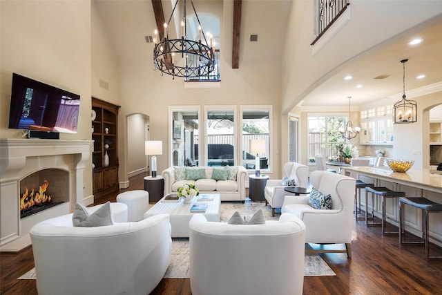 living room featuring arched walkways, an inviting chandelier, dark wood-style flooring, and a warm lit fireplace