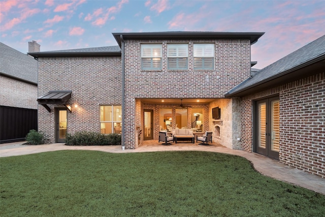 back of property at dusk with outdoor lounge area, a patio, a lawn, and brick siding