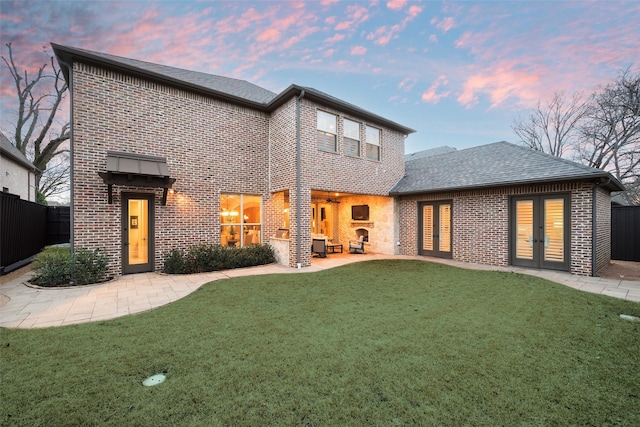 back of house featuring brick siding, fence, a lawn, french doors, and a patio