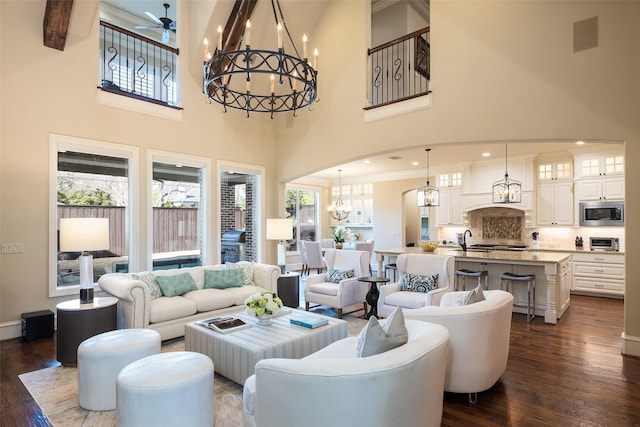 living area featuring arched walkways, a high ceiling, dark wood-style floors, and ceiling fan with notable chandelier