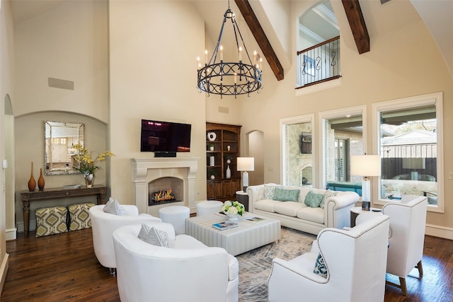 living room featuring beamed ceiling, a warm lit fireplace, wood finished floors, a high ceiling, and a chandelier