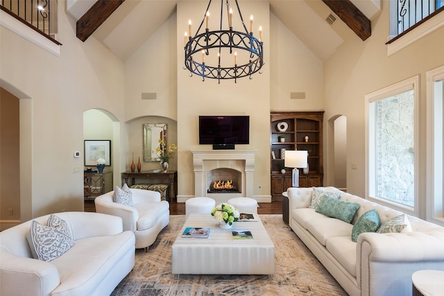 living room with visible vents, high vaulted ceiling, beam ceiling, arched walkways, and a warm lit fireplace