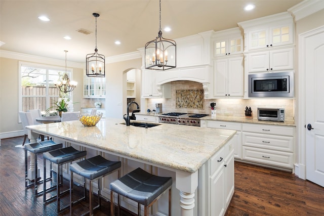 kitchen featuring stainless steel microwave, a sink, ornamental molding, arched walkways, and range