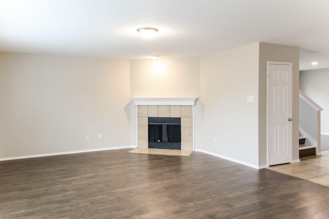 unfurnished living room with stairway, a tile fireplace, baseboards, and wood finished floors