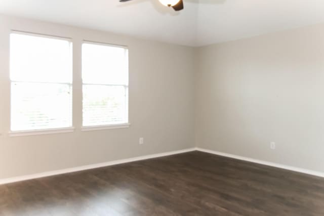 empty room with dark wood-style floors, ceiling fan, and baseboards