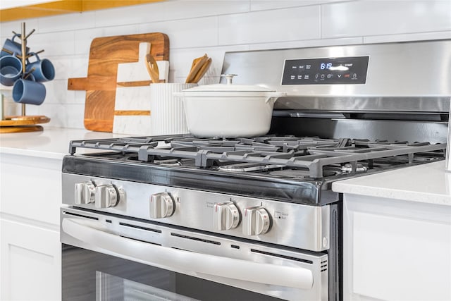 room details featuring tasteful backsplash, stainless steel gas range oven, white cabinetry, and light countertops