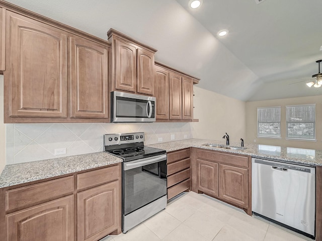 kitchen with light stone counters, lofted ceiling, a sink, decorative backsplash, and appliances with stainless steel finishes