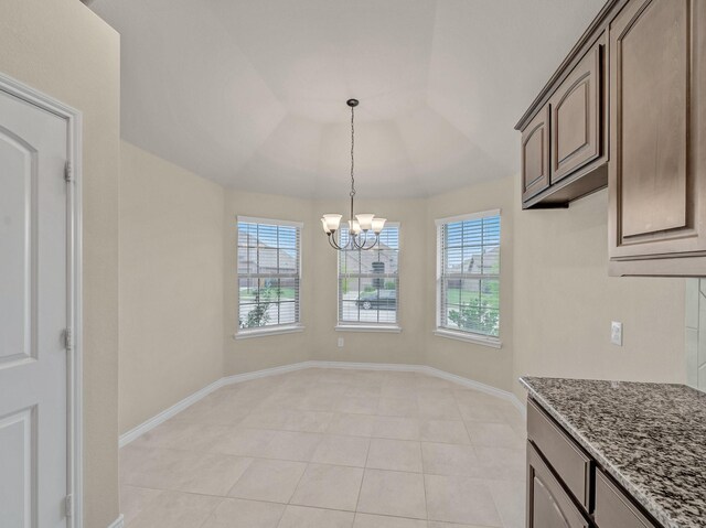 unfurnished dining area featuring baseboards, a notable chandelier, a raised ceiling, and light tile patterned flooring