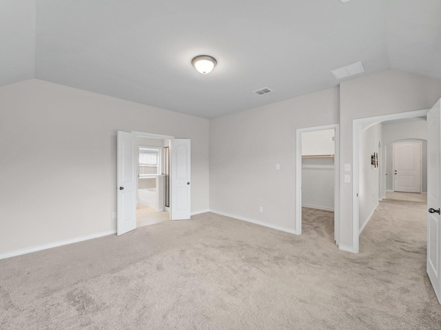 empty room featuring visible vents, arched walkways, light colored carpet, and lofted ceiling