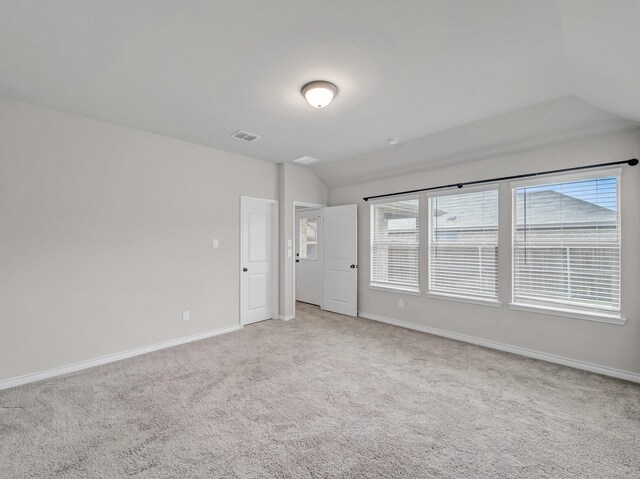 spare room with visible vents, baseboards, light colored carpet, and vaulted ceiling