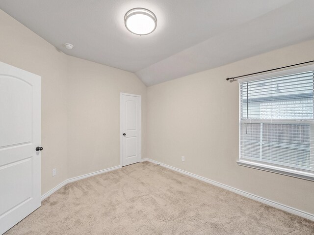 empty room with vaulted ceiling, light colored carpet, and baseboards