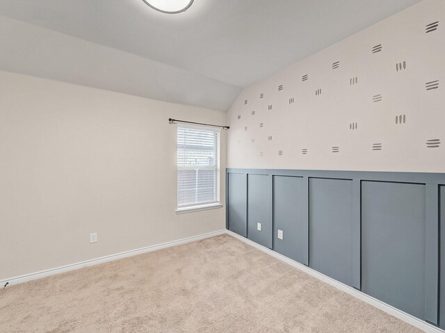 empty room with vaulted ceiling, a decorative wall, carpet, and a wainscoted wall