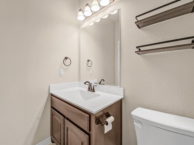 half bath featuring toilet, vanity, and a textured wall